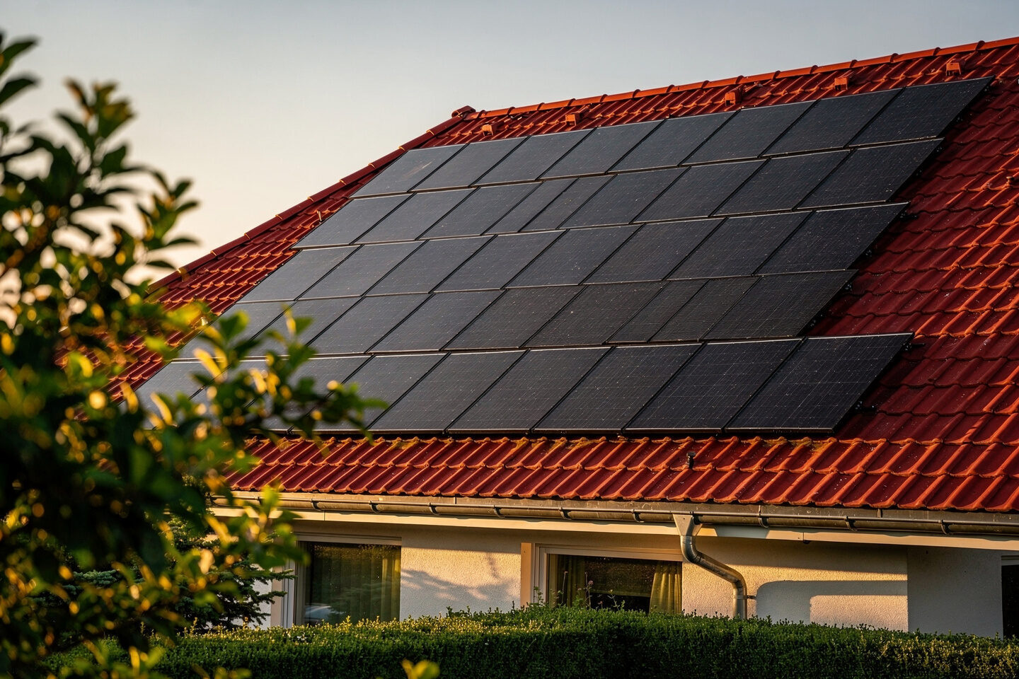 Photovoltaikanlage mit schwarzen Modulen auf rotem Ziegeldach eines Einfamilienhauses